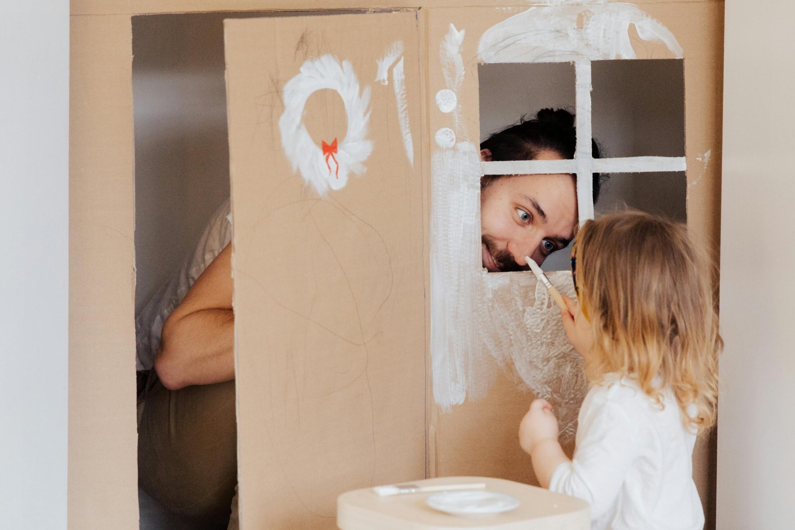 Father and daughter enjoying creative bonding by painting a cardboard playhouse indoors.